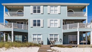 A two-story beachfront building with balconies, a wooden walkway, and outdoor seating. - Gulf-front home on the beach with 3-tier deck, Gulf views & pool access (Orange Beach)
