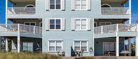 A two-story beachfront building with balconies, a wooden walkway, and outdoor seating.