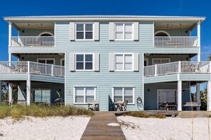 A two-story beachfront building with balconies, a wooden walkway, and outdoor seating. - Gulf-front home on the beach with 3-tier deck, Gulf views & pool access (Orange Beach)