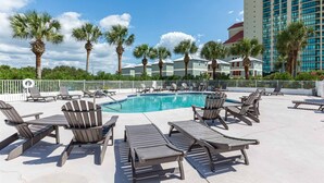 A pool area with lounge chairs, palm trees, and a high-rise building in the background. - Gulf-front home on the beach with 3-tier deck, Gulf views & pool access (Orange Beach)