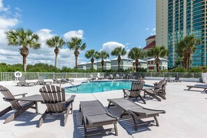 A pool area with lounge chairs, palm trees, and a high-rise building in the background. - Gulf-front home on the beach with 3-tier deck, Gulf views & pool access (Orange Beach)