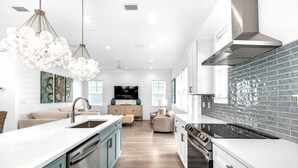 A modern kitchen with a central island, stainless steel appliances, and a backsplash of dark tiles. - Azure! Sleeps 22 ! Golf Cart ! Beach Access ! Pool! (Destin)