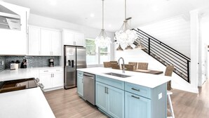 A modern kitchen with white cabinets, a stainless steel refrigerator, and a central island with a sink. - Azure! Sleeps 22 ! Golf Cart ! Beach Access ! Pool! (Destin)