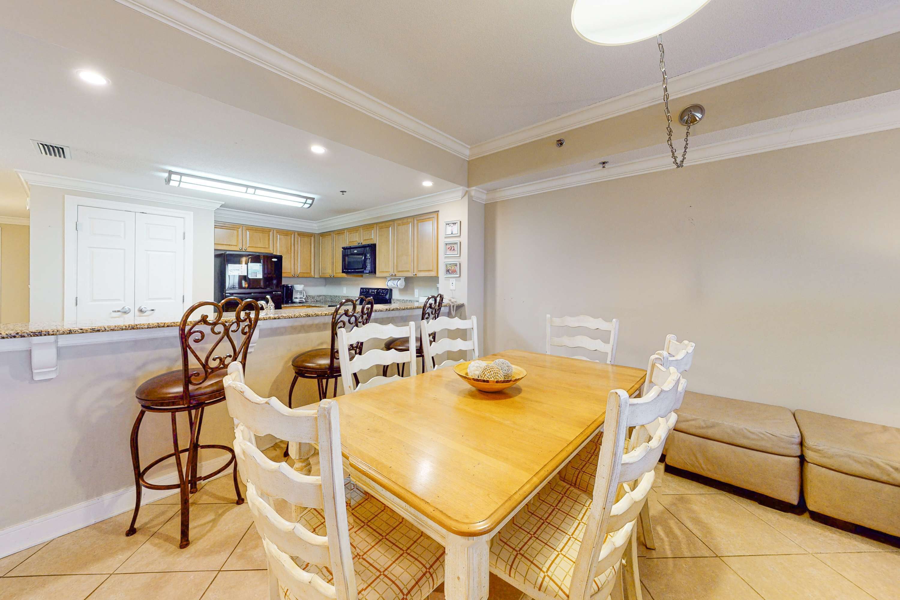 A dining area with a wooden table and white chairs, a kitchen in the background, and a beige sofa.