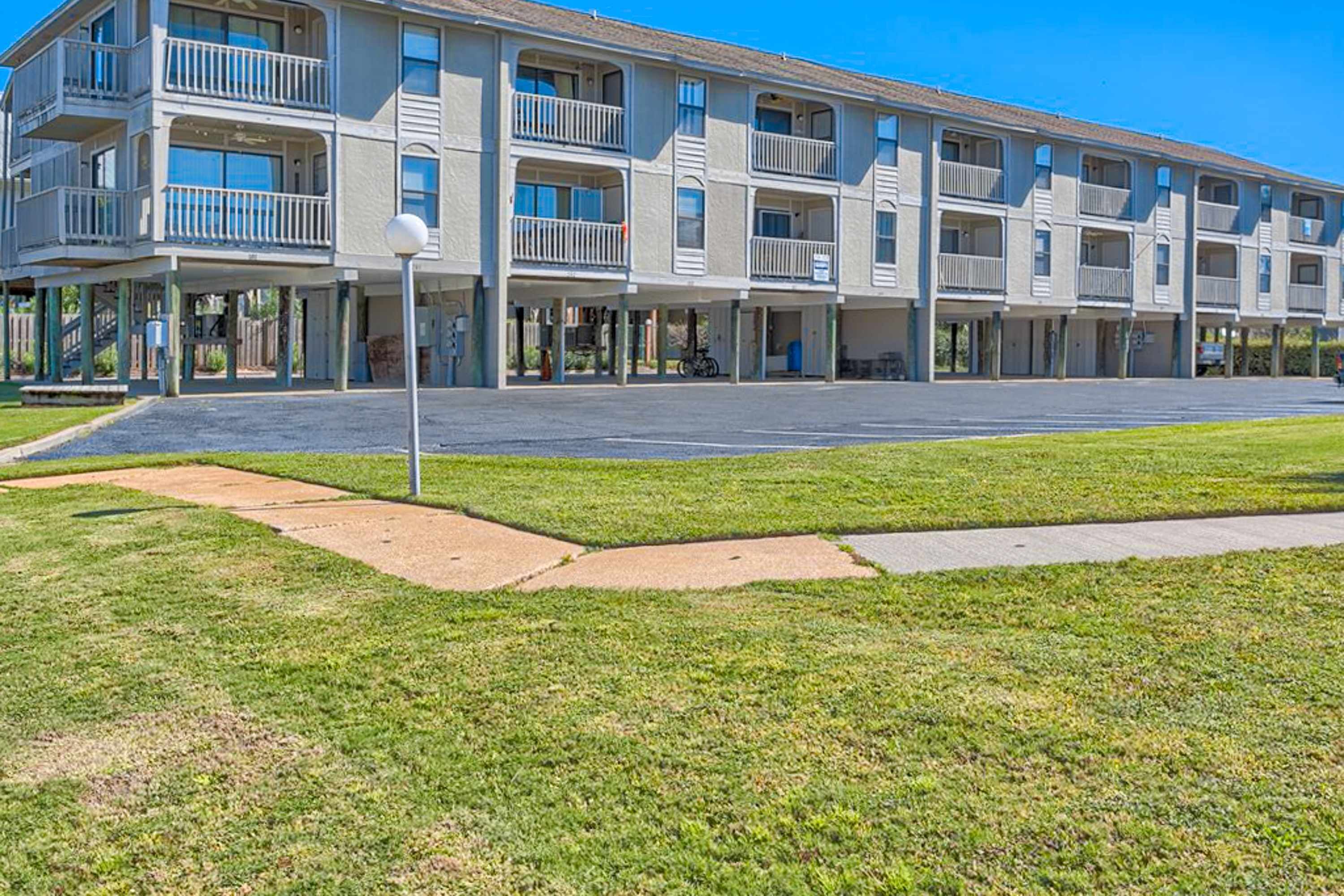 A multi-story motel with balconies, a parking lot, and a grassy area.