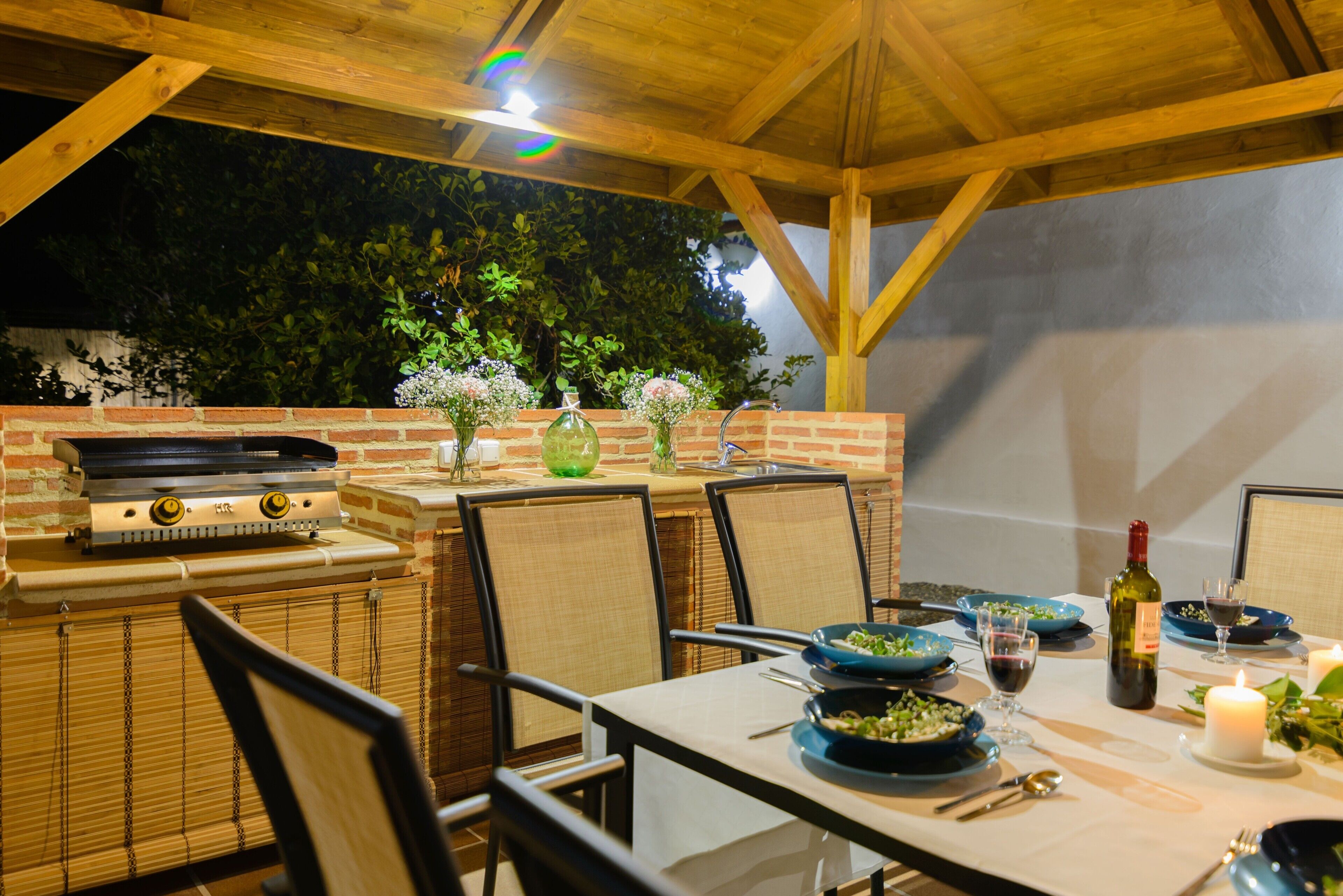Un área de comedor al aire libre con una parrilla de ladrillo, sillas de mimbre y una mesa preparada para una comida.