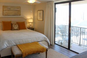 Une chambre à coucher comprenant un lit, un banc, une table de chevet, une lampe, un tableau encadré et un balcon avec des chaises.