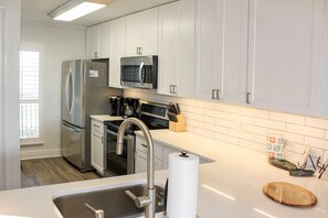 A modern kitchen with stainless steel appliances, white cabinets, and a wooden cutting board on the counter. - Coastal escape with 2 water-view balconies, 2 pools, tennis & beach access (Orange Beach)
