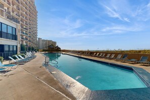 A swimming pool with lounge chairs, a building with balconies, and a clear sky. - Gulf-front escape with pools & gym - walk to beach & dining (Orange Beach)