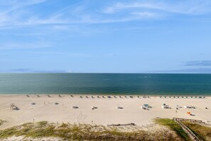 A beach with rows of umbrellas and lounge chairs, a lifeguard tower, and a clear view of the ocean. - Gulf-front escape with pools & gym - walk to beach & dining (Orange Beach)