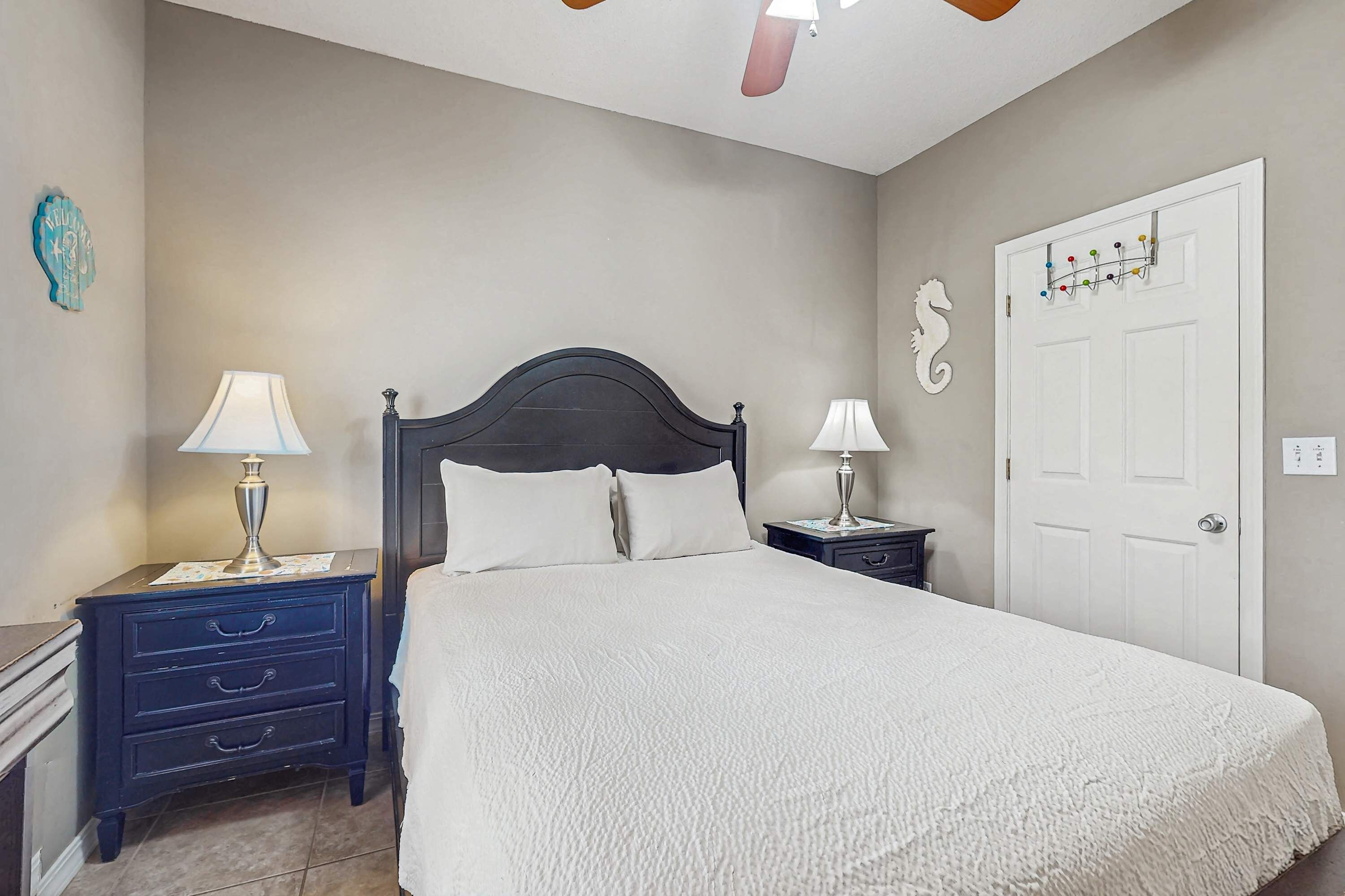 Une chambre à coucher avec un grand lit, deux tables de chevet avec des lampes, une commode, une porte blanche et une horloge murale.