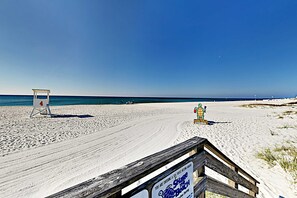 A beach with a wooden boardwalk, a lifeguard tower, and a sign indicating a turtle watching area. - Spacious condo with pool & screened porch (Orange Beach)