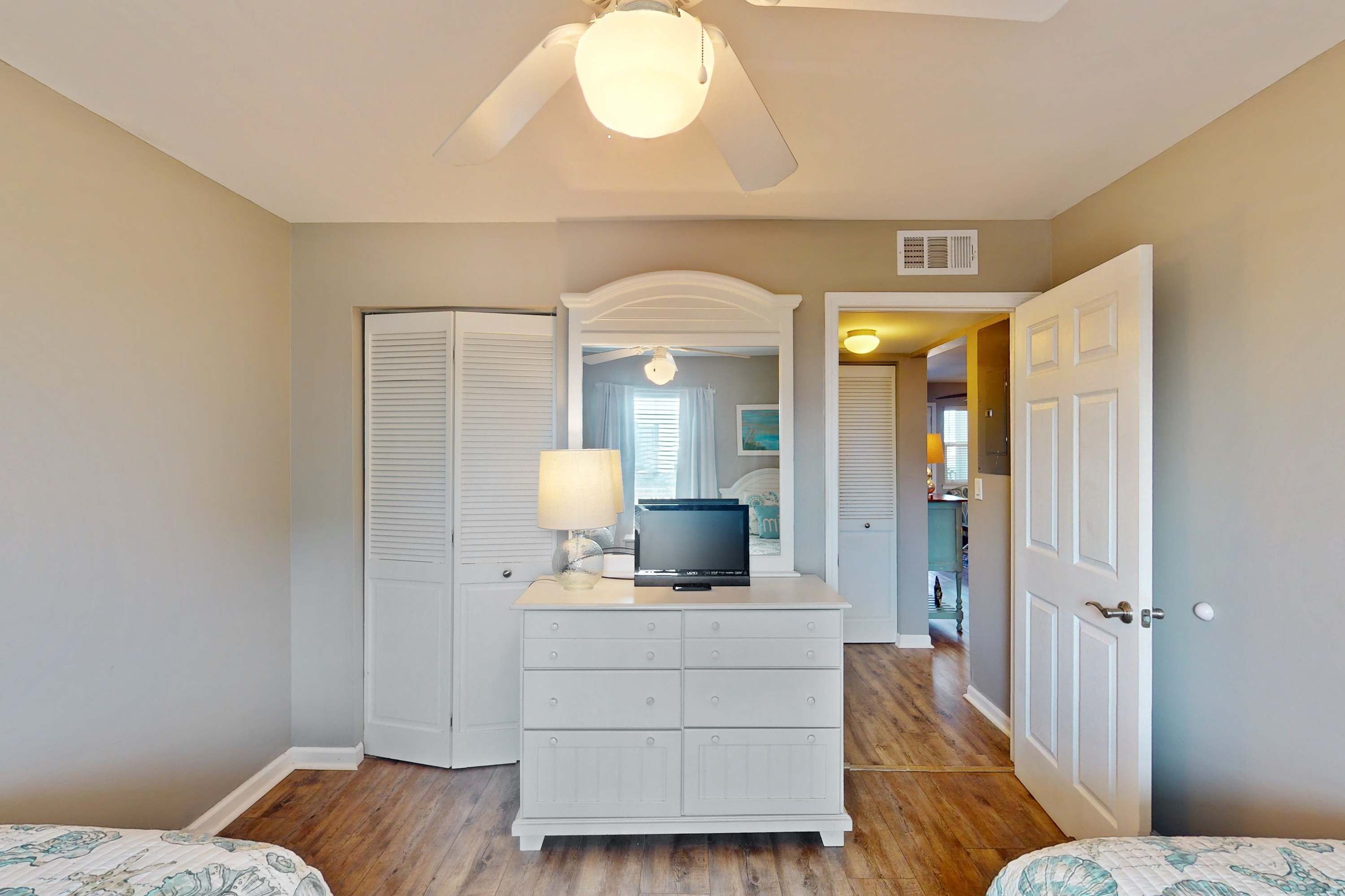 A bedroom with a bed, a dresser, a ceiling fan, and a door leading to another room.