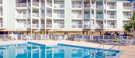 A hotel with a pool, multiple balconies, and a covered area with lounge chairs.