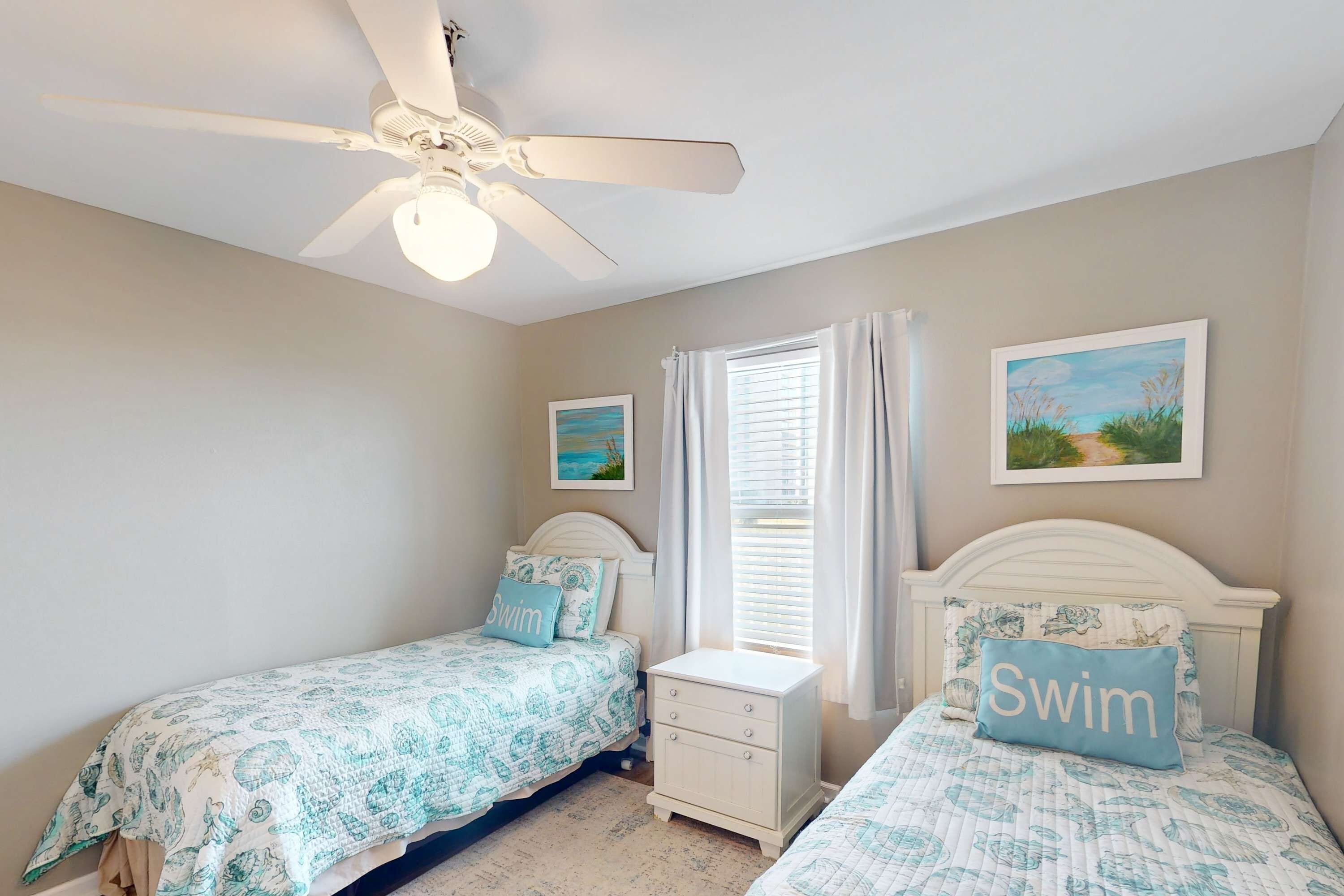 A bedroom with two beds, a ceiling fan, a window with curtains, and two wall-mounted pictures.
