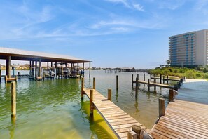 A waterfront hotel with a dock, a covered seating area, and a large building in the background. - Updated condo with Gulf & river views & pool - across from beach & near dining (Orange Beach)