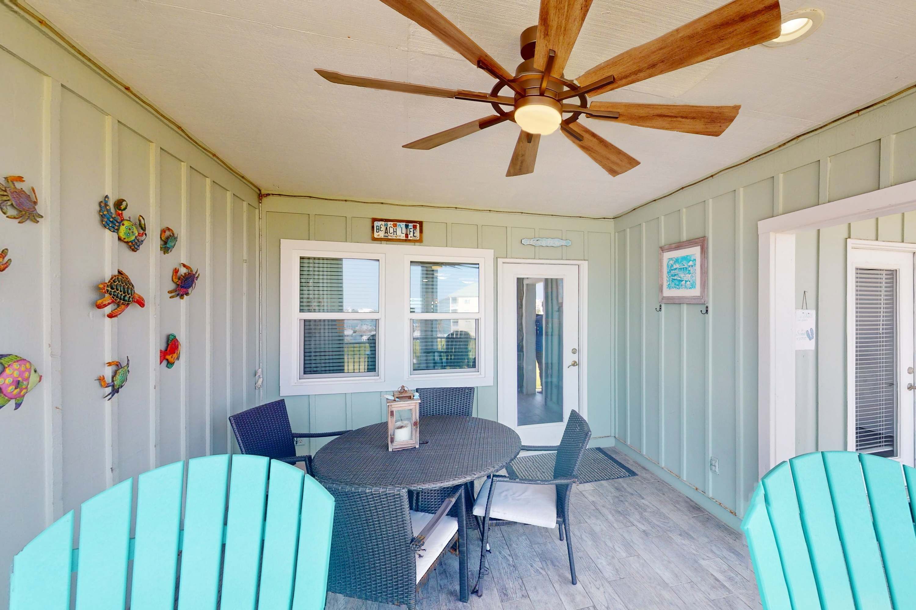 A covered patio with a ceiling fan, a round table with chairs, and decorative wall art.