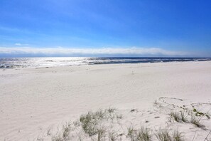 A beach with sand dunes, sparse vegetation, and a clear sky. - Coastal condo with special fall & winter rates (Orange Beach)