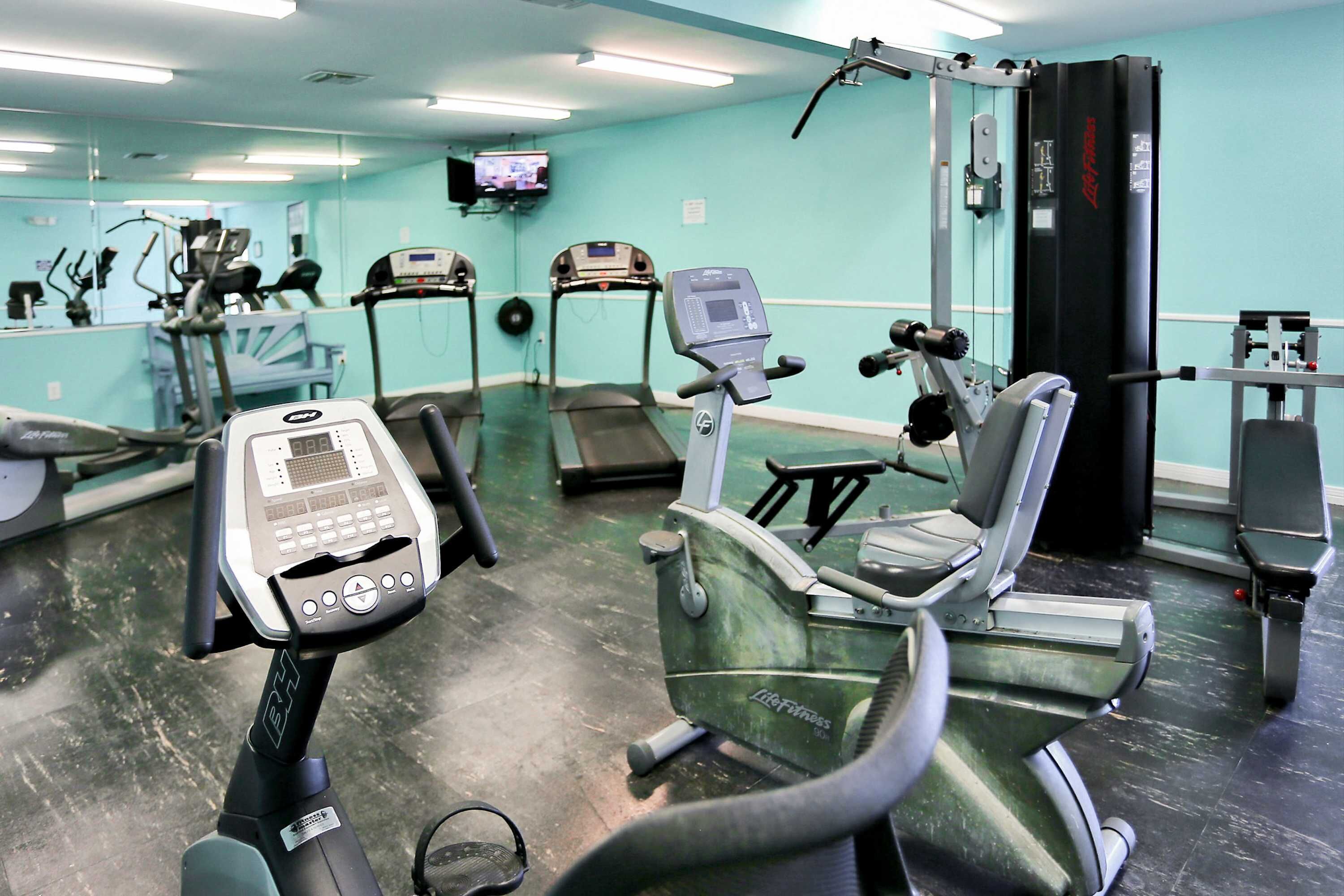 Una palestra con attrezzature per esercizi, una TV e uno specchio a parete.