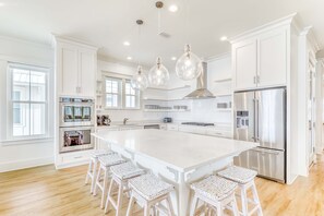 A spacious kitchen with a large island, white cabinetry, stainless steel appliances, and hanging pendant lights. - Luxurious Gulf-front home w private plunge pool, steps from the beach (Orange Beach)
