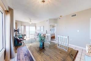 A spacious living area with a wooden dining table, a potted plant, and a white railing. - Beachfront vacation home with spacious balconies, beach access, pools & hot tub (Orange Beach)