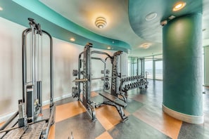 A gym with weightlifting equipment, a bench, and dumbbells. - Gulf-front condo with pool, tennis, lazy river & private hot tub (Orange Beach)