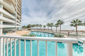 A hotel with a pool, palm trees, and a beach view. - Gulf-front condo with pool, tennis, lazy river & private hot tub (Orange Beach)