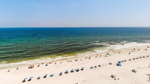 Een strand met rijen ligbedden en parasols, een heldere lucht en een rustige zee.