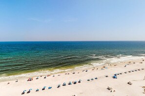 Ein Strand mit Reihen von Liegen und Sonnenschirmen, einem klaren Himmel und ruhiger See.