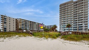 Een strandhotel met meerdere balkons, een zandstrand en een wimpelstok met vlaggen.