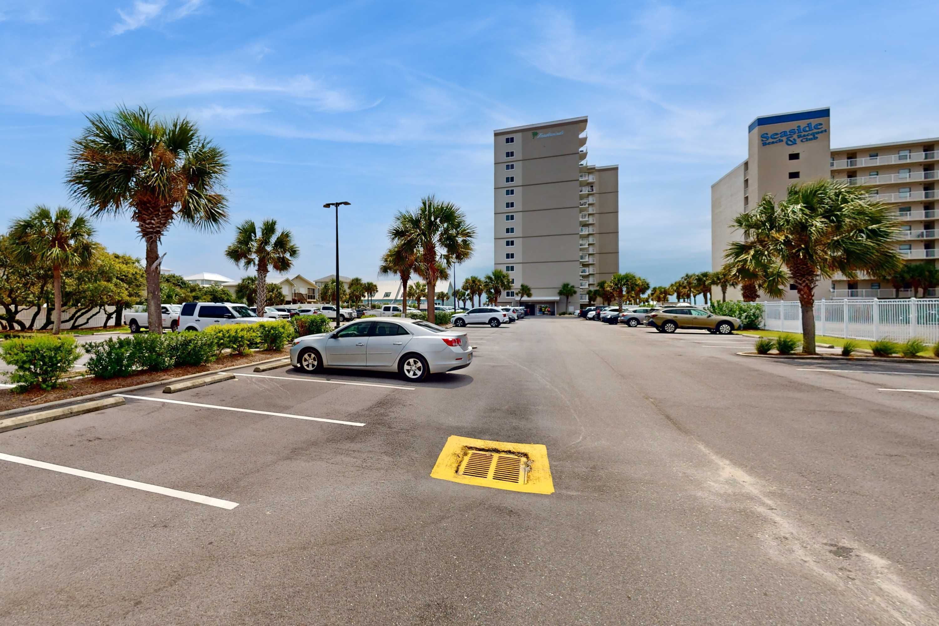 A parking lot with multiple cars, palm trees, and a hotel building with a sign.