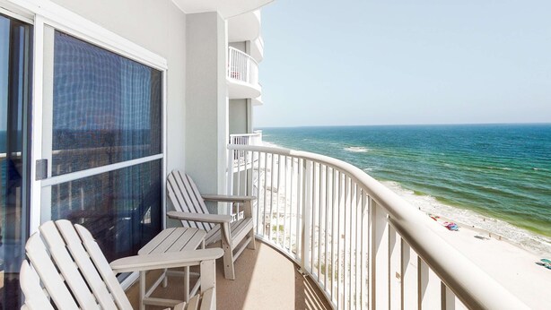 Een balkon met witte stoelen, een glazen deur en uitzicht op de oceaan.
