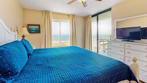 Camera d'hotel con un letto, una televisione, una ventola a soffitto, una finestra con tende e vista sull'oceano.