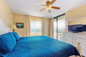 A hotel room with a bed, a television, a ceiling fan, a window with curtains, and a view of the ocean. - Waterfront condo w/ an open dining & living area, private balcony, shared pools (Orange Beach)