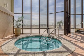 A hot tub with a view of a fence and palm trees through large windows. - Waterfront condo w/ an open dining & living area, private balcony, shared pools (Orange Beach)