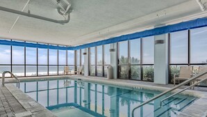 An indoor swimming pool with clear glass walls, a view of the sky, and a tiled floor. - Beachfront condo w/ private, corner balcony, community pools, & a grilling area (Orange Beach)