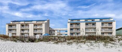 Et hotel ved stranden med flere balkoner og en sandstrand i forgrunden.