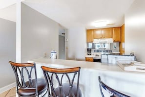 A modern kitchen with wooden cabinets, a central island, and a seating area with metal chairs.
