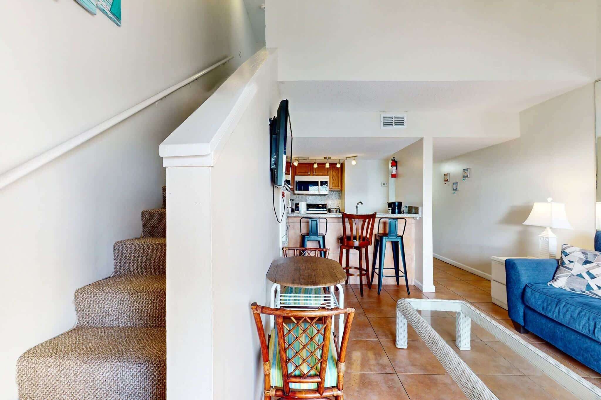 A living room with a blue sofa, a coffee table, and a staircase leading to a kitchen area with wooden cabinets and a microwave.