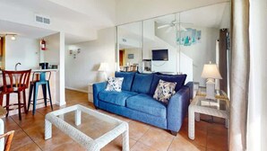 A living room with a blue sofa, a glass coffee table, and a dining area with chairs and a table.