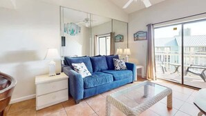 A living room with a blue sofa, a glass coffee table, a white nightstand, a lamp, and a large mirror.