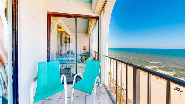 A balcony with two chairs, a glass door leading to an interior room, and a view of the sea. - Gulf front condo with pools/hot tub - ocean view, covered balcony & washer/dryer (Orange Beach)
