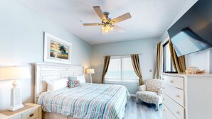 A bedroom with a bed, a ceiling fan, a window with curtains, a chair, a dresser, and a TV. - Gulf front condo with pools/hot tub - ocean view, covered balcony & washer/dryer (Orange Beach)