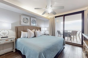 Ein Schlafzimmer mit einem Bett, Nachttischen, einem Deckenventilator, Kunstwerken und einem Balkon mit Stühlen.