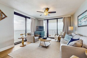 Ein geräumiges Wohnzimmer mit Deckenventilator, großen Fenstern, einem Fernseher und einem Balkon.