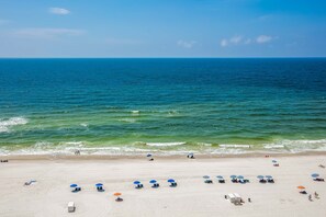 Ein Strand mit klarem, blauem Wasser, Sandufer und Sonnenschirmen.
