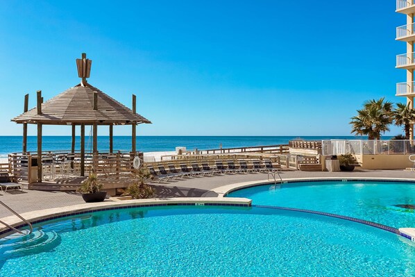 Ein Pool mit einer Holzpergola, Liegestühlen und Blick auf den Ozean.