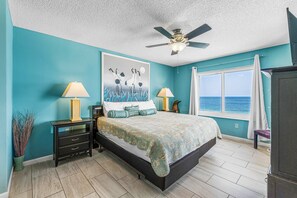 Ein Schlafzimmer mit einem Bett, zwei Nachttischen, einem Deckenventilator, einem Fenster mit Meerblick und einem Bild an der Wand.