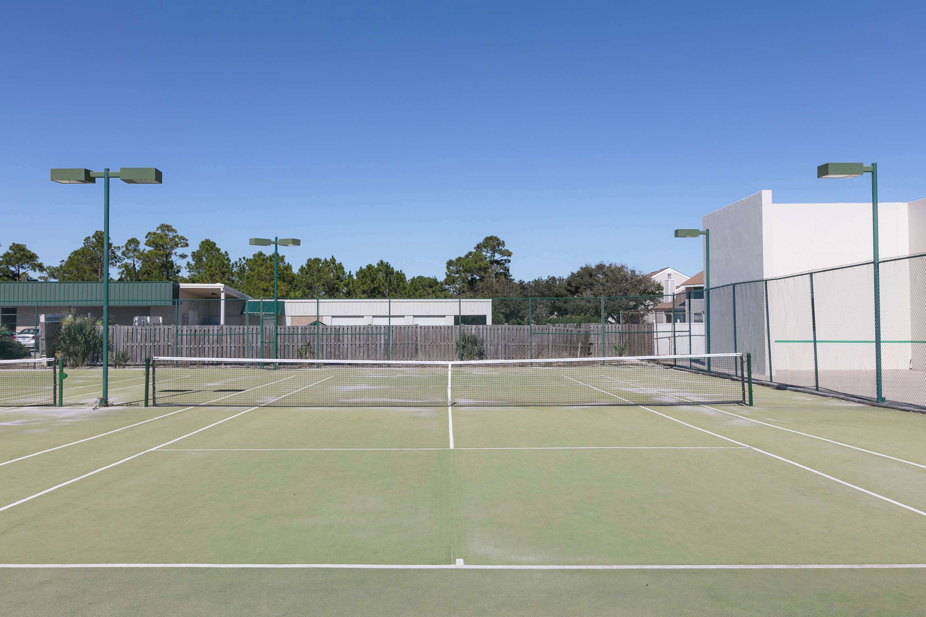 Een tennisbaan buiten met een net, groene verlichting en een hek.