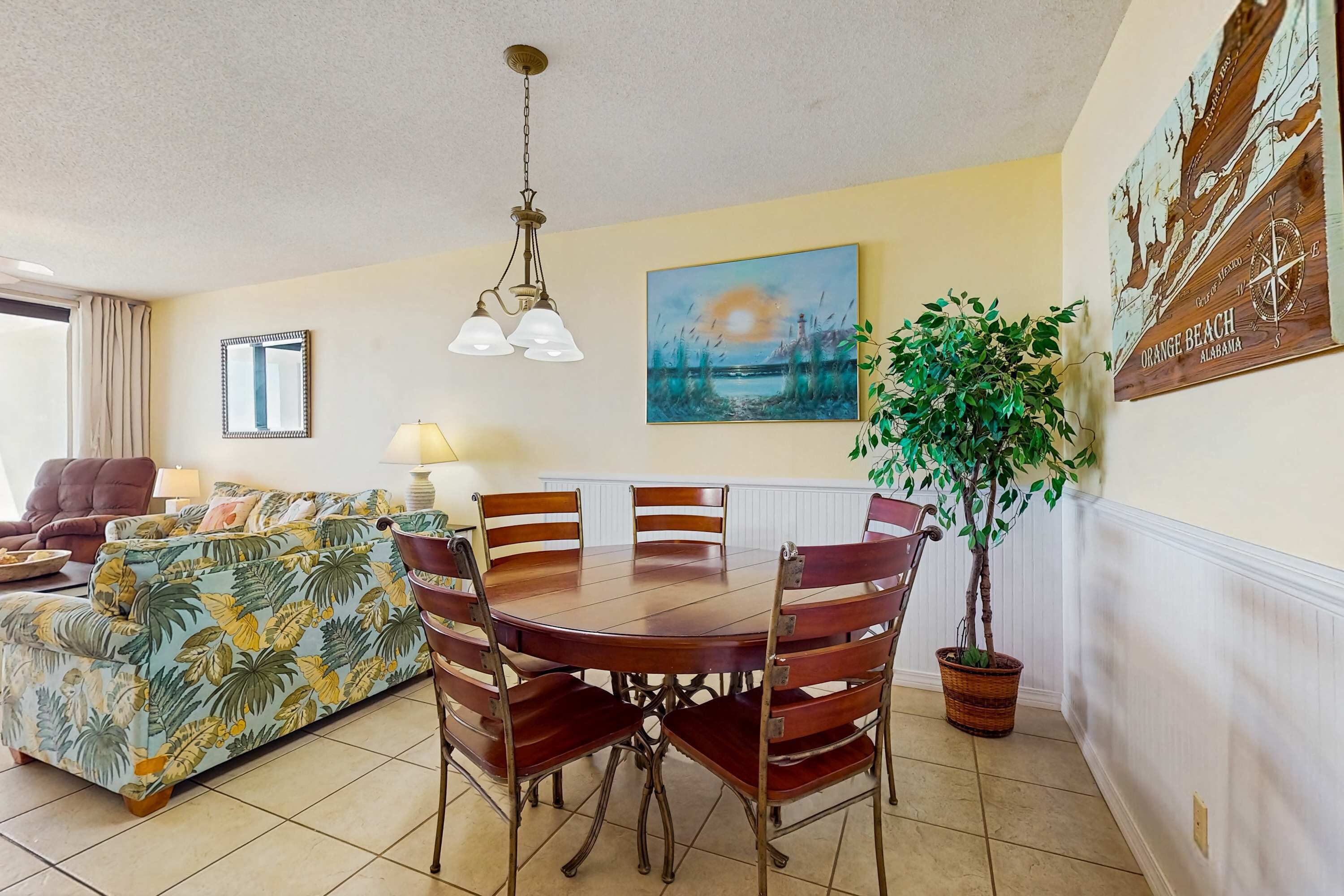 Uma sala de jantar com uma mesa redonda, cadeiras, um sofá, um abajur, um quadro e um vaso de planta.